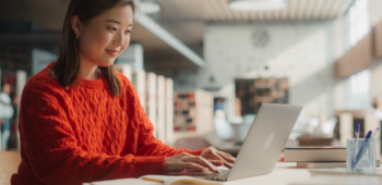 Mulher estudando no computador na biblioteca.