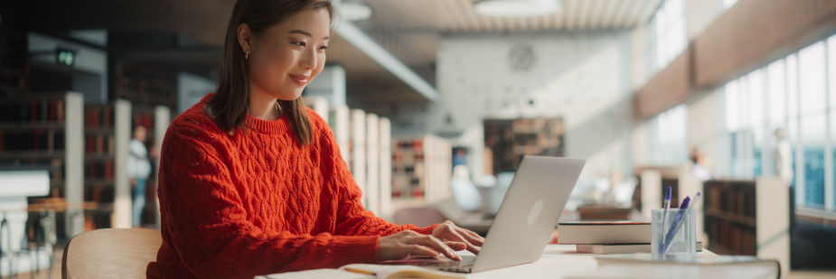 Mulher estudando no computador na biblioteca.