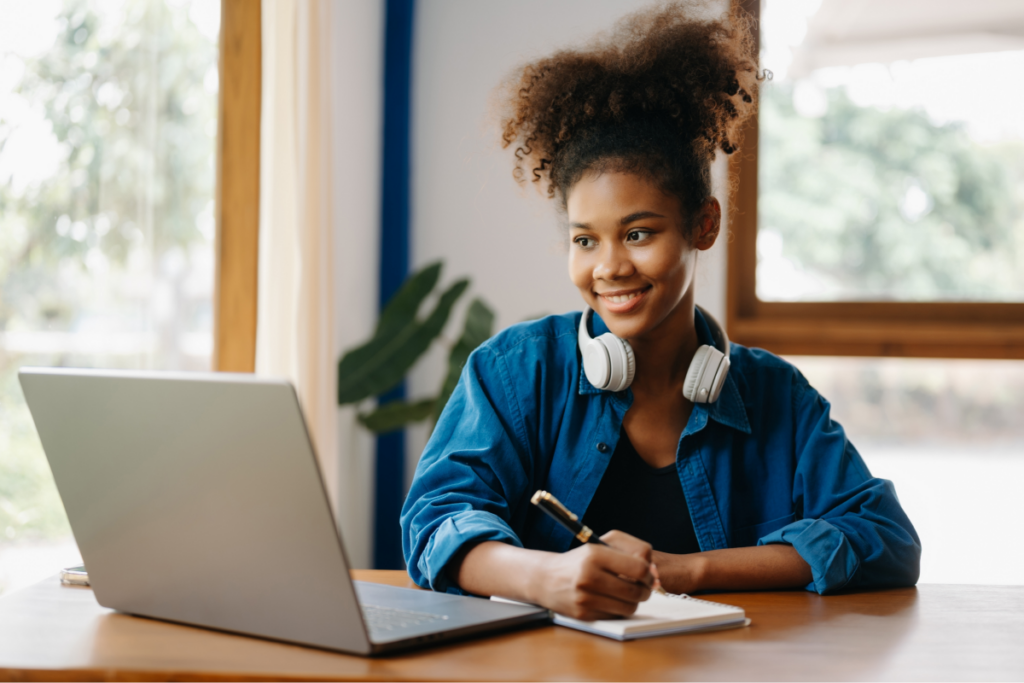 Mulher jovem estudando no computador. Ela anota algo em um caderno. Graduação tecnológica. 