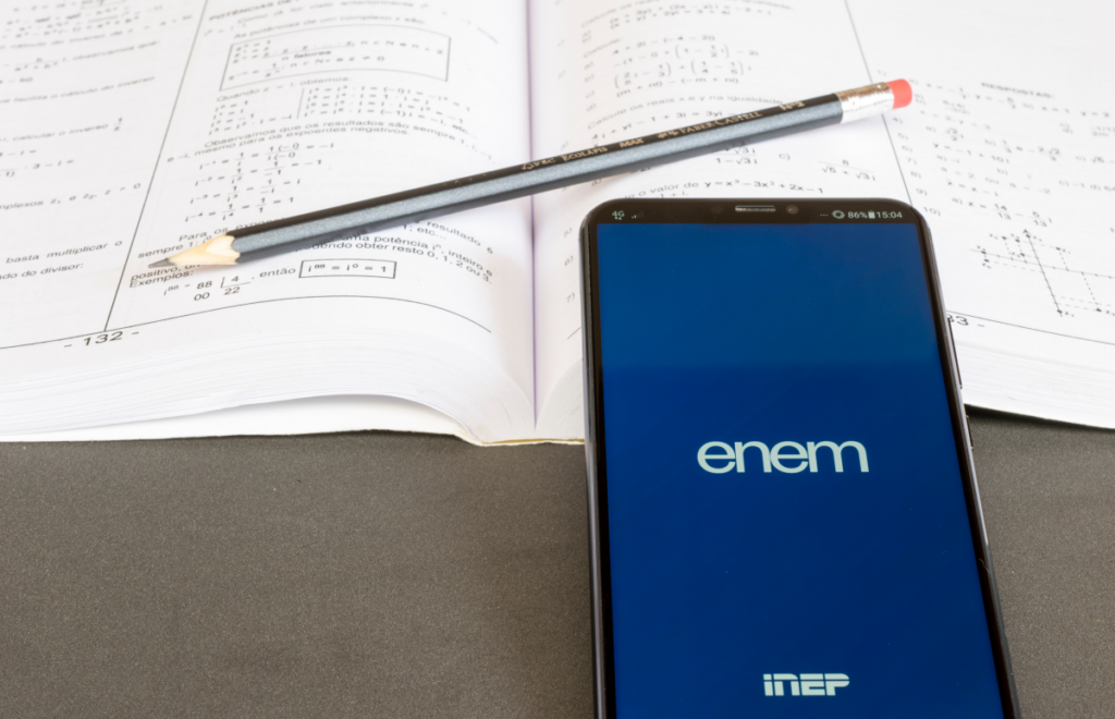 Celular mostrando a logo do Enem apoiado sobre uma prova. Como conseguir bolsa para segunda graduação.