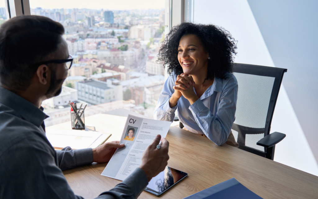 Homem segurando um currículo e entrevistando uma mulher. Como colocar graduação no currículo.