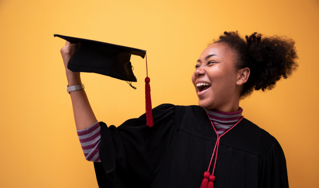 Mulher vestida de formanda e segurando um capelo. Como funciona a segunda graduação.