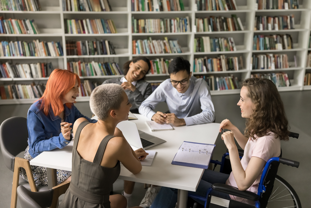 Estudantes de universidade conversando em biblioteca. Valor da faculdade de Administração em diferentes regiões e modalidades.