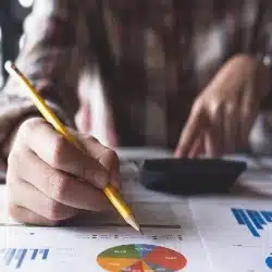 Pessoa segurando lápis em cima de papeis com gráficos