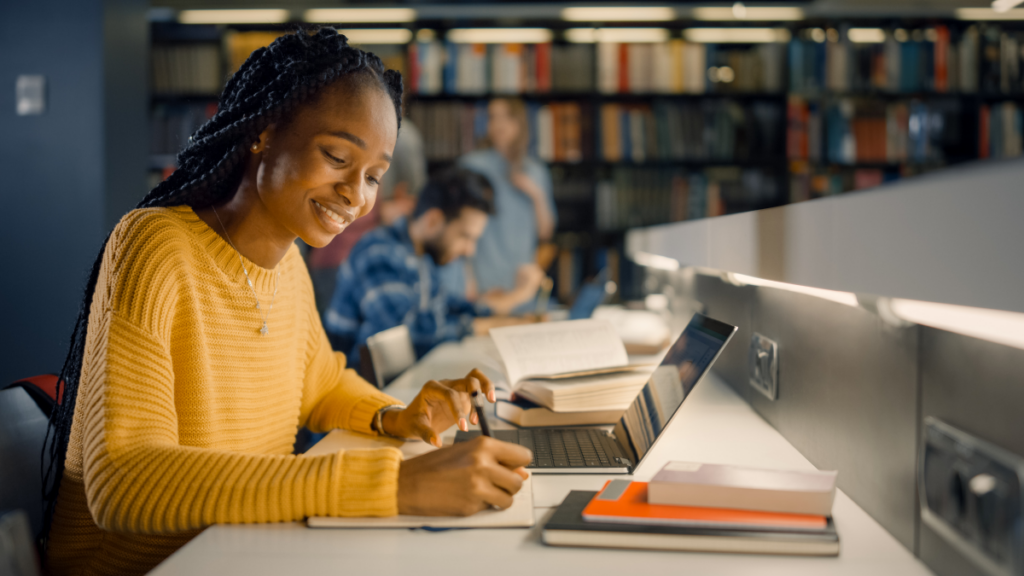 Mulher estudando no computador em uma bliblioteca.  Curso técnico ead. 
