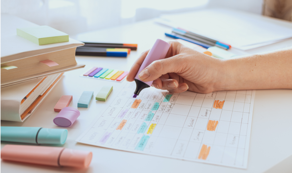 Imagem aproximada de uma mesa com materiais escolares e um cronograma de estudos. Uma mão segura uma caneta marca texto. Prova do eja.