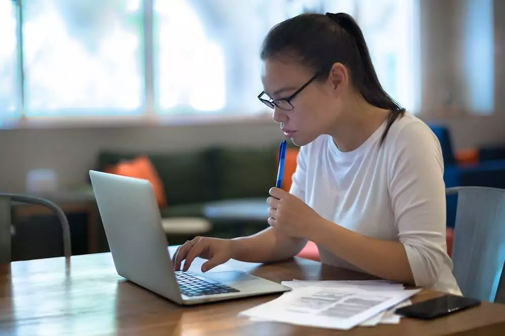 Garota pesquisando em computador com papéis ao lado