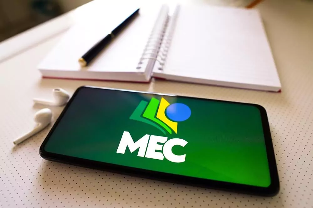 Tela do aplicativo do MEC em celular com caderno ao fundo