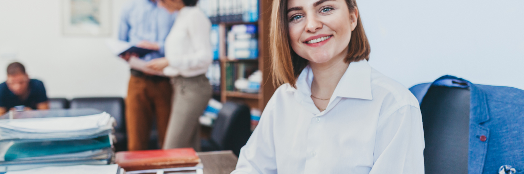 Mulher sentada à mesa em escritório com colegas ao fundo