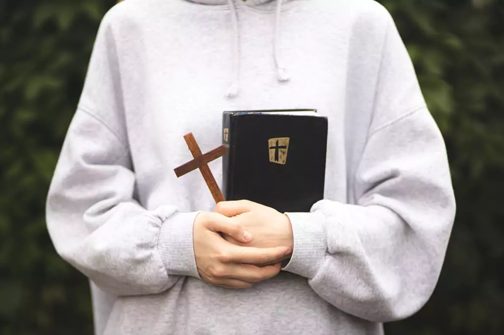Rapaz jovem segurando Bíblia e crucifixo