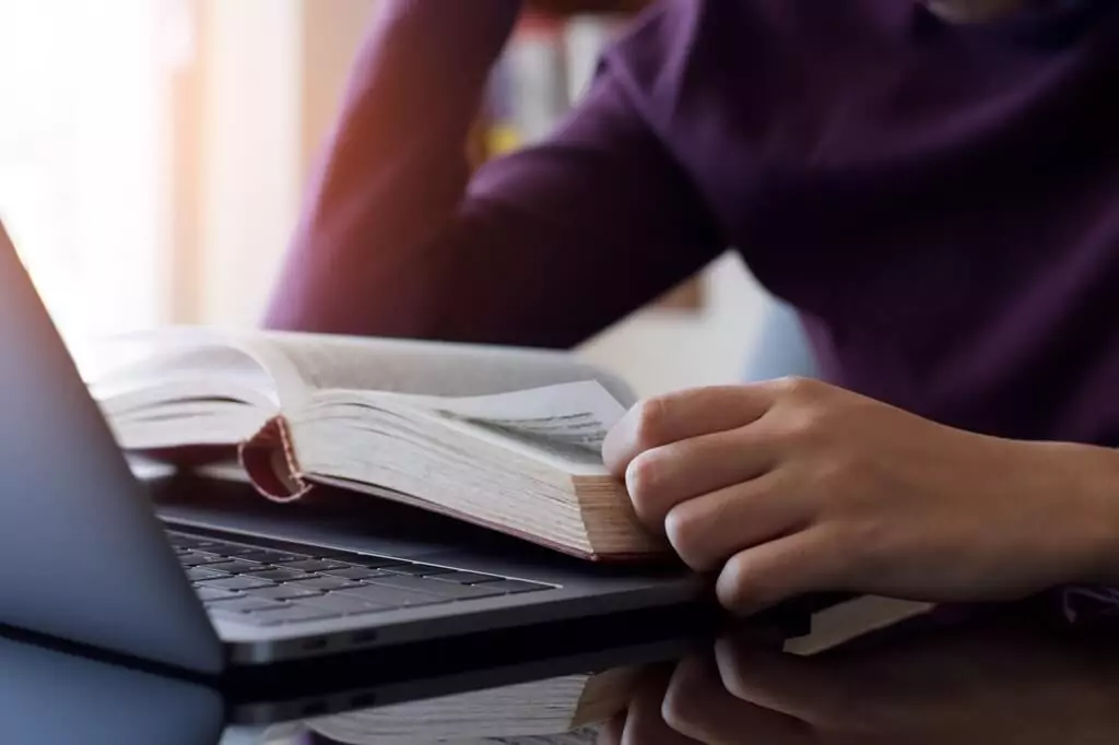 Mulher lendo livro em frente a computador