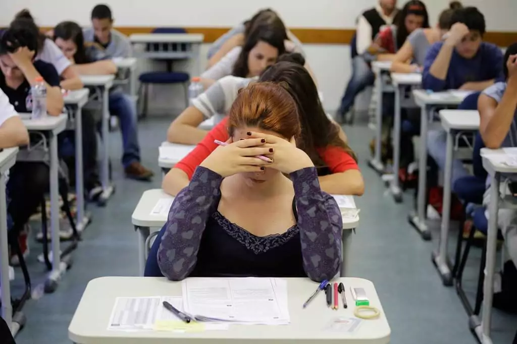 Estudante fazendo vestibular em sala com outras pessoas