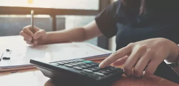 moça fazendo cálculos em calculadora e anotando