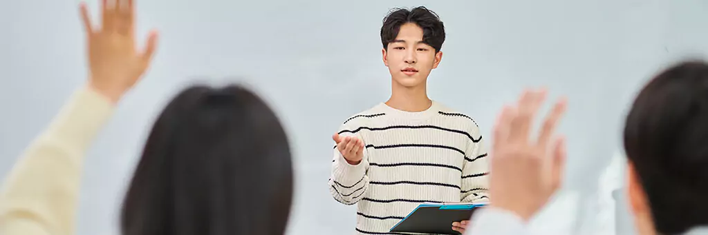 rapaz fazendo apresentação para público e sinalizando para pessoa com dúvida