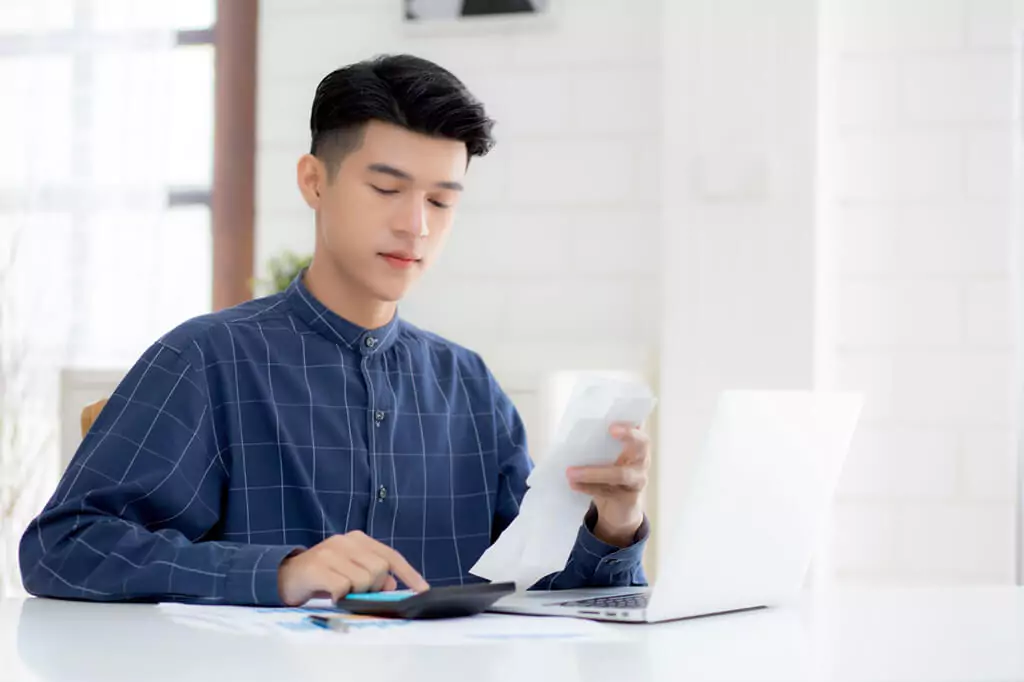 rapaz fazendo contas com calculadora e laptop