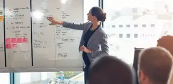 mulher dando palestra com quadro branco com anotações para pessoas em escritório