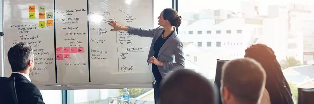 mulher dando palestra com quadro branco com anotações para pessoas em escritório