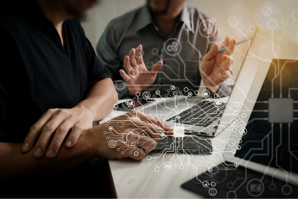 Dois colegas trabalham juntos no computador. Símbolos que remetem à tecnologia sobrepostos na foto. Jurimetria. 