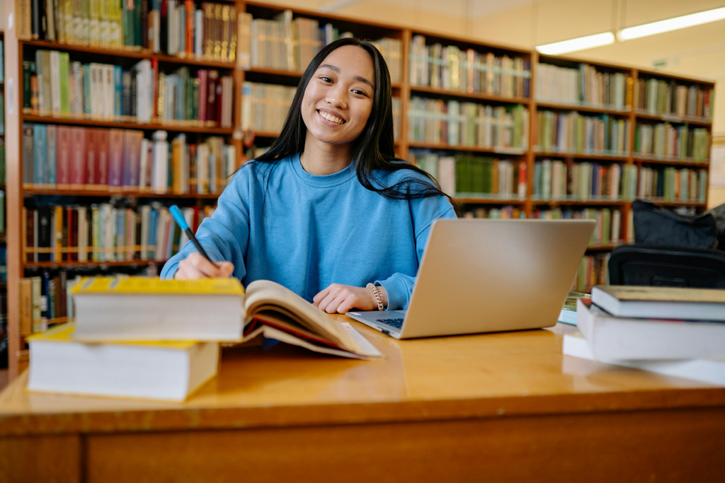 Jovem mulher estudando em biblioteca, ela sorria para a câmera. O que se aprende na faculdade de história. 