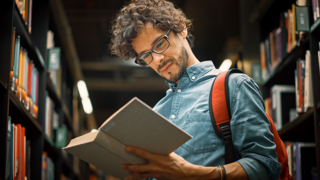 Homem lendo livro em biblioteca. O que se aprende na faculdade de história.