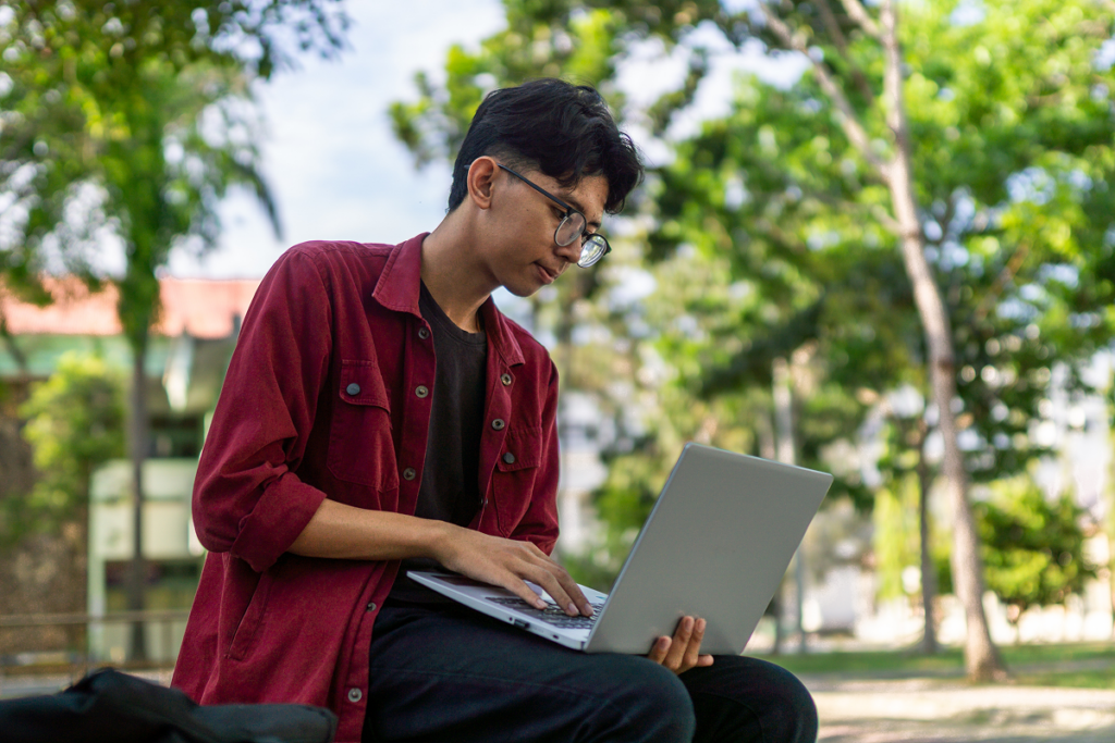 Homem jovem fazendo inscrição para o vestibular usando o computador.