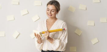 autodesenvolvimento pessoal: mulher segurando um lápis gigante e com vários post its colados na parede